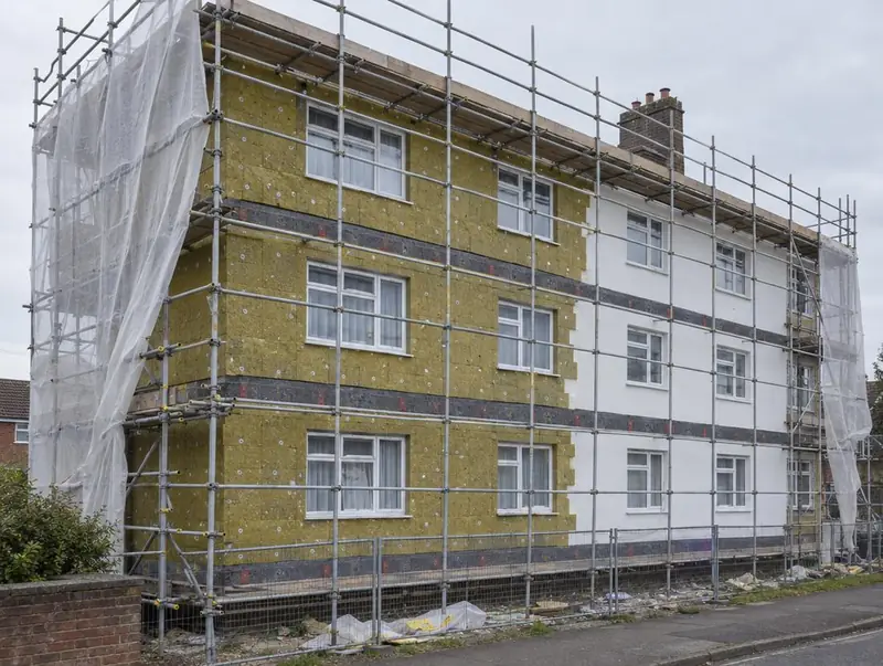 Three-storey block of flats in scaffolding with yellow mineral wool insulation and new white render