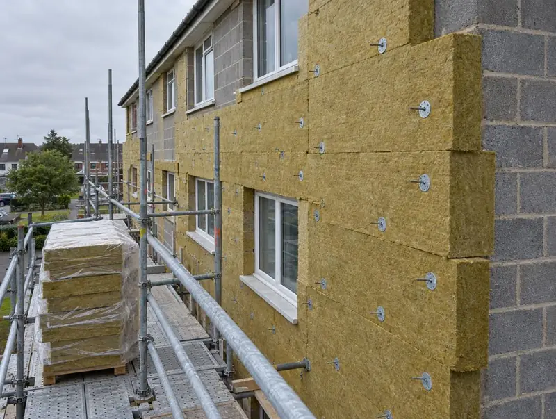 Mineral wool insulation slabs being fixed to the blockwork of a three-storey block, with wrapped slabs on the scaffold